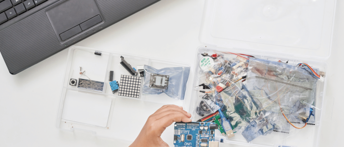 Small hand holding an Arduino with electronics parts in the background