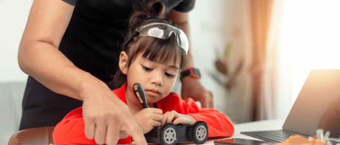 Girl working on a robot car with help from an adult