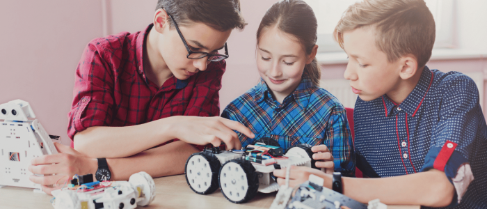 Two boys and a girl working together on several robots