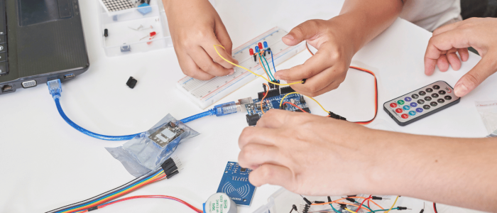 Two pairs of small hands working on electrical circuit with an Arduino
