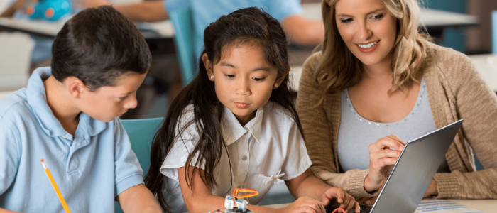 Teacher helping two elementary students program a robot with a laptop computer